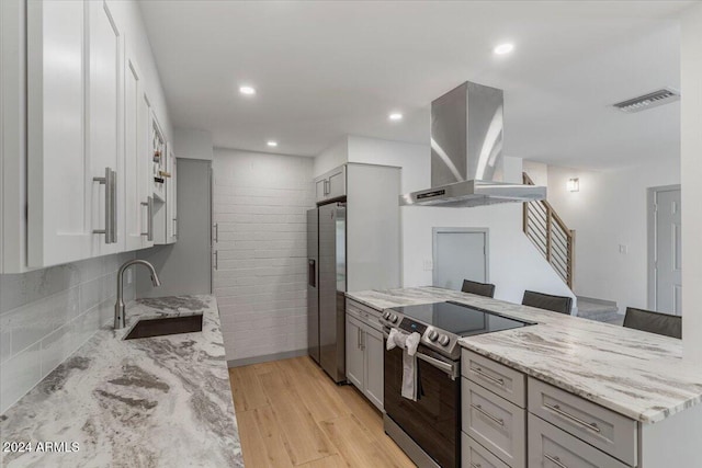 kitchen with wall chimney exhaust hood, sink, light stone countertops, and stainless steel appliances