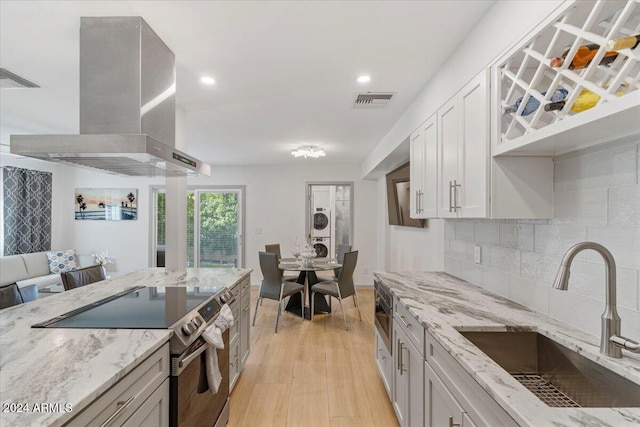 kitchen with tasteful backsplash, sink, electric stove, wall chimney range hood, and stacked washer and dryer