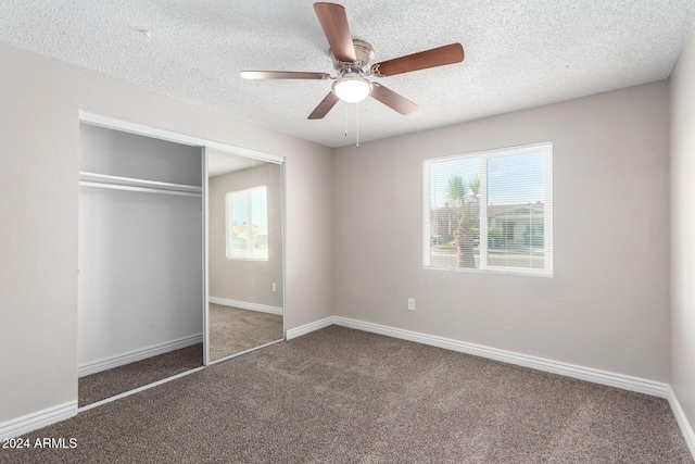 unfurnished bedroom with a textured ceiling, a closet, dark carpet, and ceiling fan