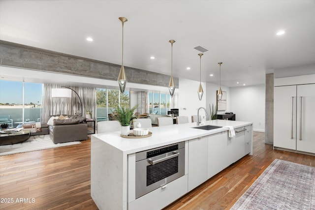 kitchen with sink, oven, white cabinets, an island with sink, and pendant lighting