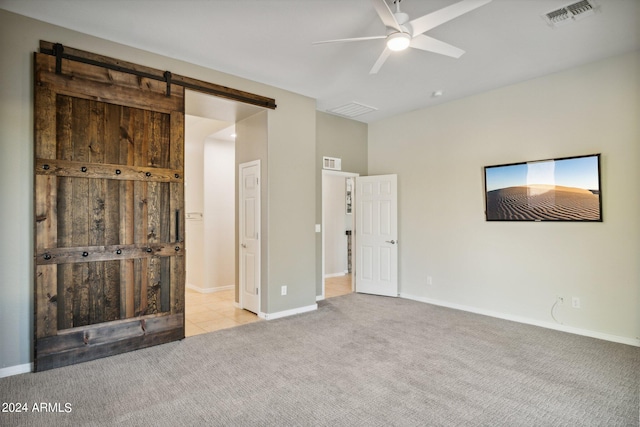 unfurnished bedroom with a barn door, ceiling fan, and light colored carpet