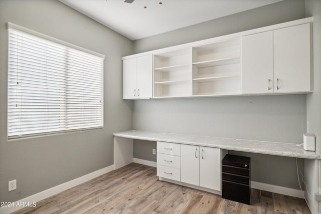 unfurnished office featuring built in desk, ceiling fan, and light hardwood / wood-style floors