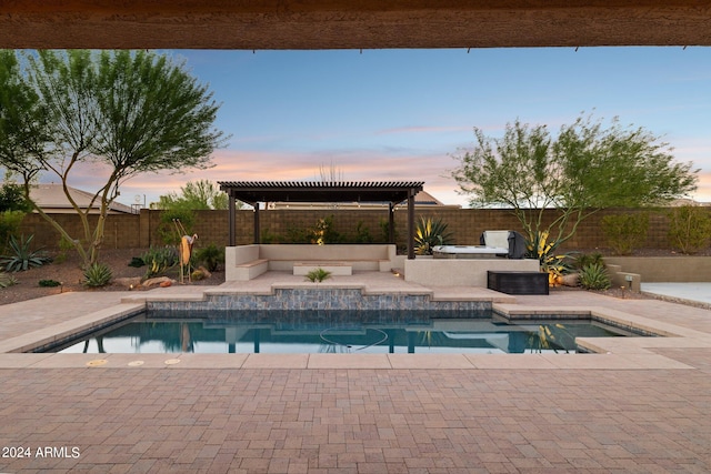 pool at dusk featuring exterior kitchen, a patio area, and a pergola