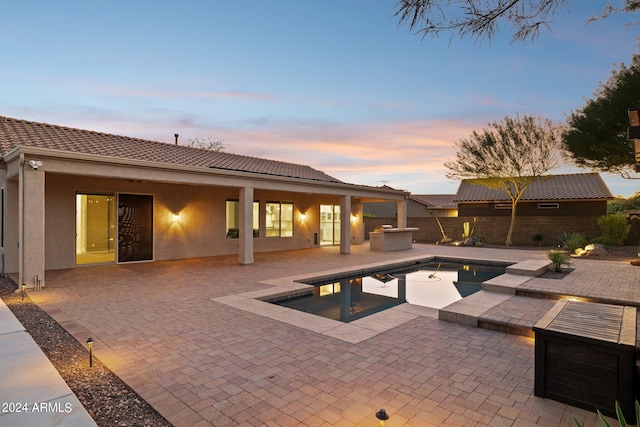 pool at dusk featuring a hot tub and a patio