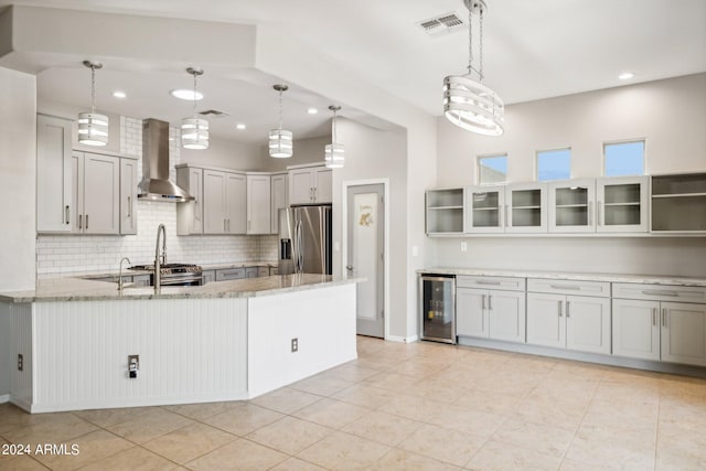 kitchen with light stone countertops, stainless steel appliances, wall chimney range hood, kitchen peninsula, and beverage cooler