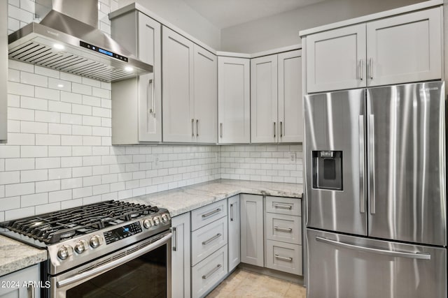 kitchen with wall chimney exhaust hood, appliances with stainless steel finishes, tasteful backsplash, and light stone countertops