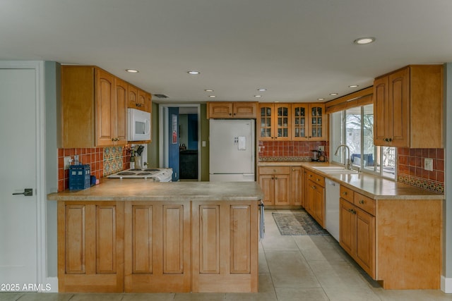kitchen featuring light countertops, glass insert cabinets, a sink, white appliances, and a peninsula
