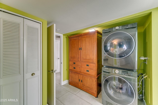 clothes washing area featuring stacked washer and dryer, laundry area, baseboards, and light tile patterned floors