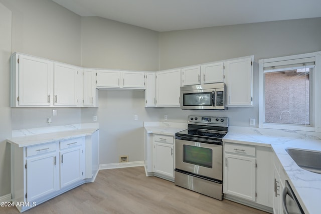 kitchen with light stone countertops, white cabinetry, light hardwood / wood-style floors, and appliances with stainless steel finishes