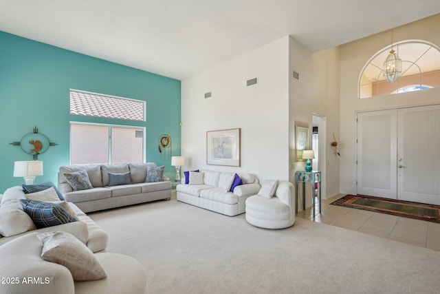 tiled living room with carpet, visible vents, a notable chandelier, and a high ceiling