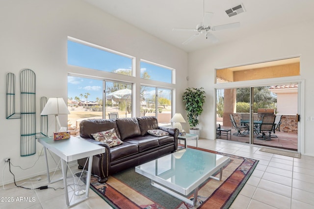 living room with a wealth of natural light, light tile patterned flooring, visible vents, and a towering ceiling