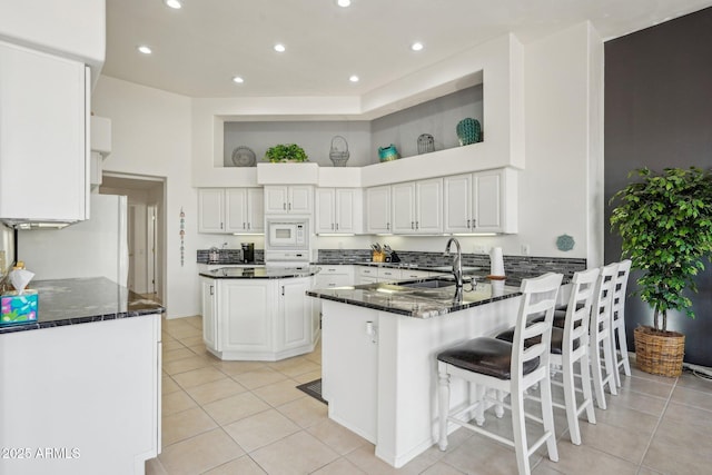 kitchen featuring light tile patterned flooring, a peninsula, white appliances, a sink, and white cabinetry