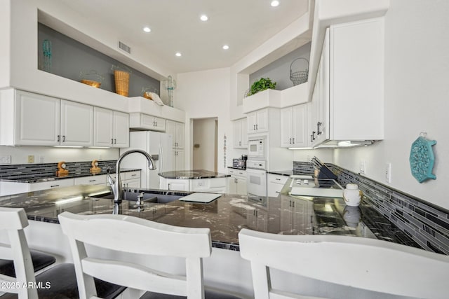 kitchen featuring white appliances, a center island, white cabinetry, a sink, and recessed lighting