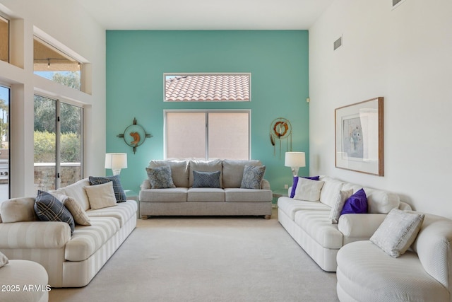 living area with carpet floors, a towering ceiling, and visible vents