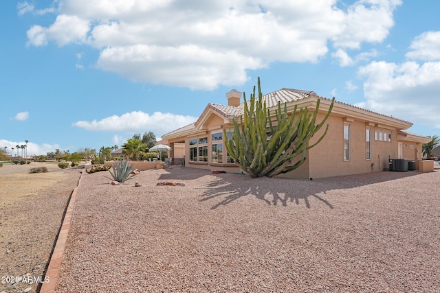 back of property featuring a patio, central air condition unit, a tile roof, stucco siding, and a chimney