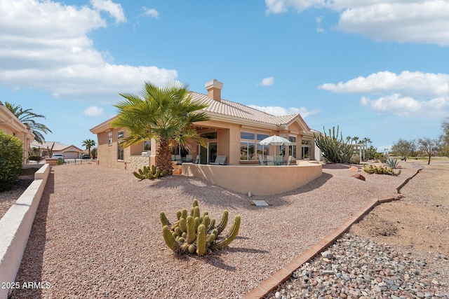 back of house featuring a patio area, a tile roof, a chimney, and stucco siding