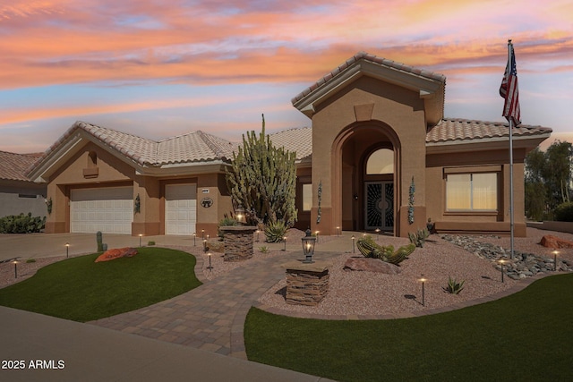 mediterranean / spanish home with a garage, driveway, a tile roof, and stucco siding