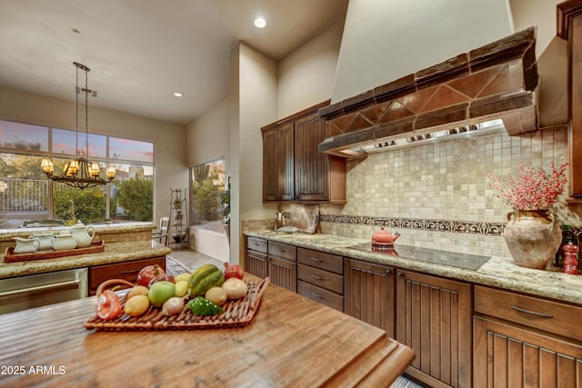 9534 E Monument Dr, Scottsdale, AZ 85262 - kitchen featuring black electric stovetop, wall chimney exhaust hood, tasteful backsplash, a chandelier, and hanging light fixtures
