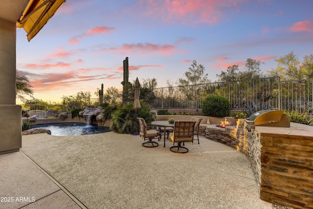 9534 E Monument Dr, Scottsdale, AZ 85262 - patio terrace at dusk featuring an outdoor fire pit, exterior kitchen, a patio area, and a fenced backyard