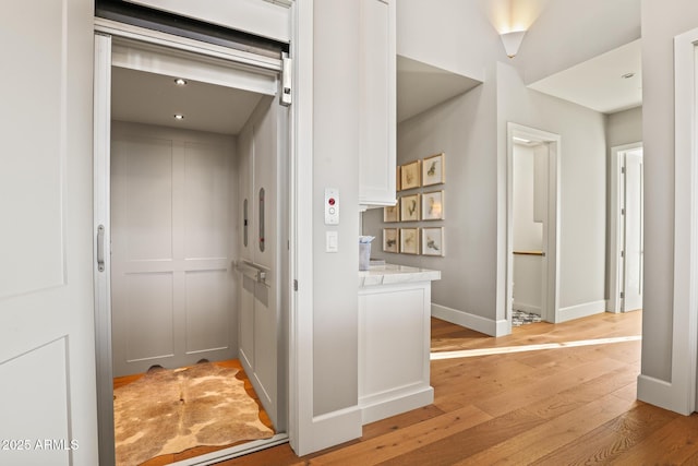 hall with baseboards, light wood-type flooring, and elevator