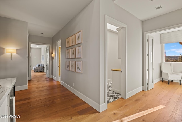 hall featuring light wood finished floors, baseboards, and visible vents