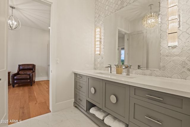 bathroom with baseboards, marble finish floor, a notable chandelier, vanity, and backsplash