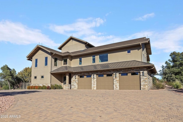 view of front of home featuring an attached garage, stone siding, decorative driveway, and a standing seam roof