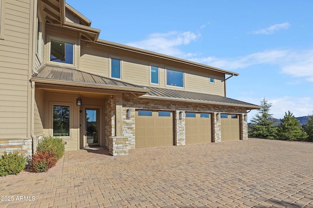 multi unit property featuring stone siding, metal roof, an attached garage, a standing seam roof, and decorative driveway