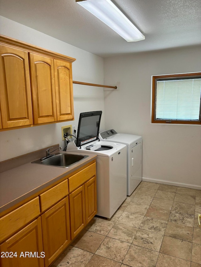 laundry area featuring washing machine and clothes dryer, sink, light tile floors, cabinets, and a textured ceiling