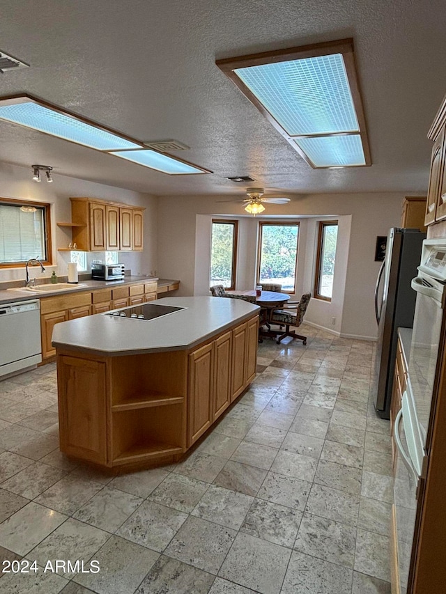 kitchen with ceiling fan, light tile floors, a textured ceiling, dishwasher, and an island with sink