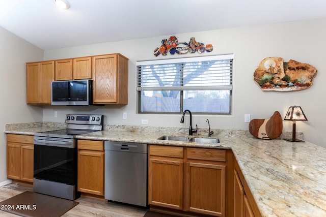 kitchen with lofted ceiling, sink, light stone countertops, light hardwood / wood-style floors, and stainless steel appliances