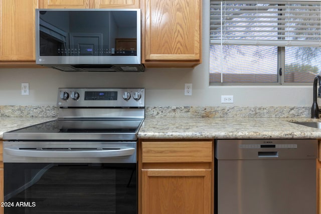 kitchen with stainless steel appliances, light stone counters, and sink