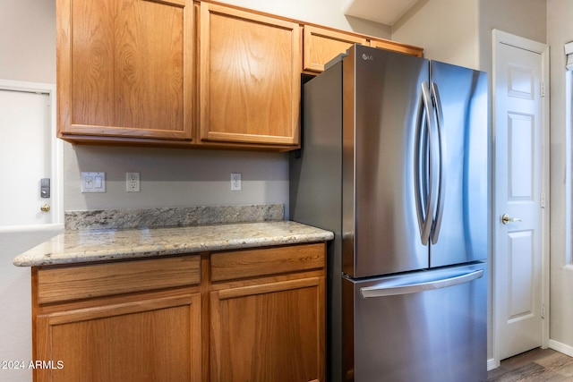 kitchen with light stone countertops, hardwood / wood-style flooring, and stainless steel refrigerator