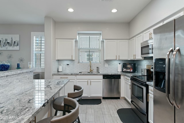 kitchen featuring appliances with stainless steel finishes, tasteful backsplash, sink, white cabinets, and light stone countertops