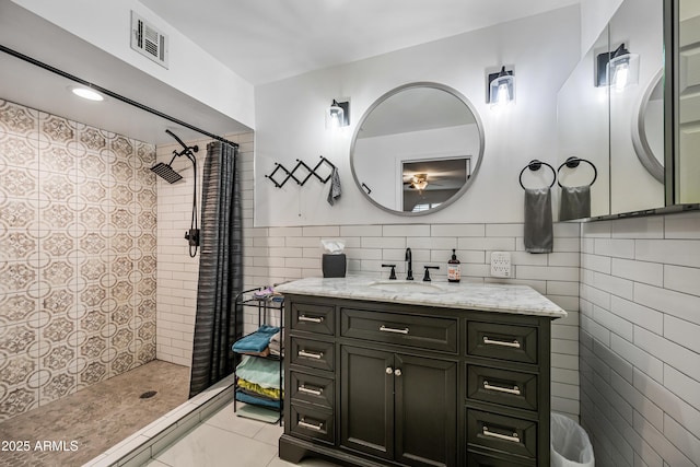 bathroom with tile patterned floors, vanity, tile walls, and a tile shower