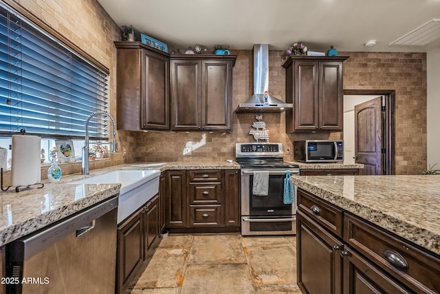 kitchen with wall chimney range hood, stainless steel appliances, dark brown cabinetry, light stone countertops, and decorative backsplash