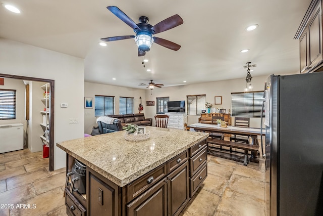 kitchen featuring dark brown cabinets, stainless steel fridge, light stone countertops, and a kitchen island