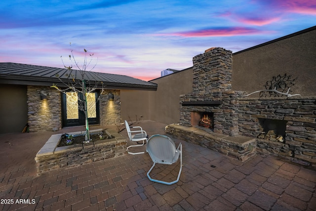 patio terrace at dusk featuring an outdoor stone fireplace