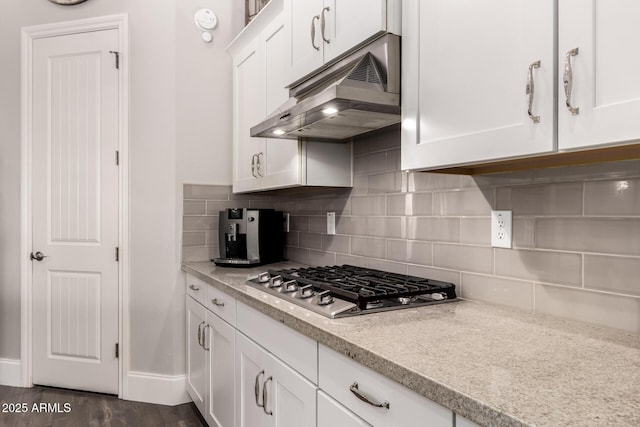 kitchen with dark wood finished floors, under cabinet range hood, stainless steel gas stovetop, white cabinetry, and backsplash