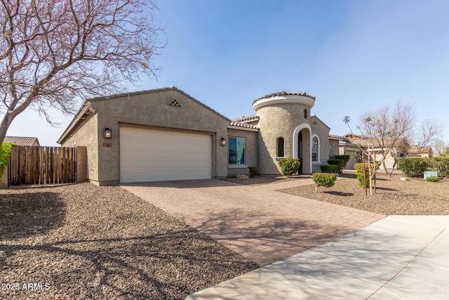 mediterranean / spanish home featuring a tiled roof, an attached garage, fence, decorative driveway, and stucco siding