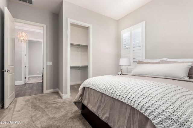 carpeted bedroom featuring a walk in closet, a closet, baseboards, and an inviting chandelier