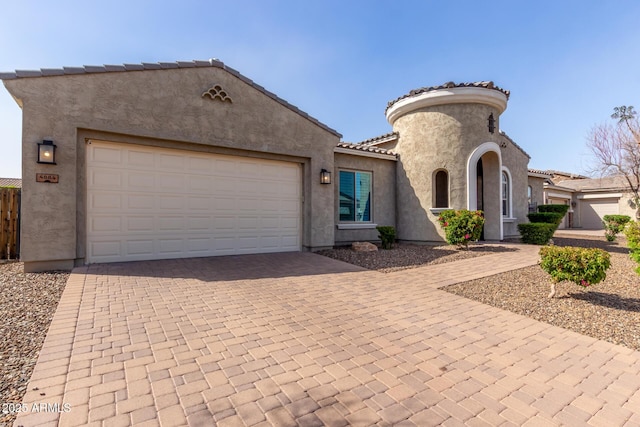 view of front of house with decorative driveway, a tile roof, an attached garage, and stucco siding