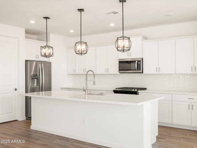 kitchen with stainless steel appliances, a center island with sink, white cabinetry, and pendant lighting