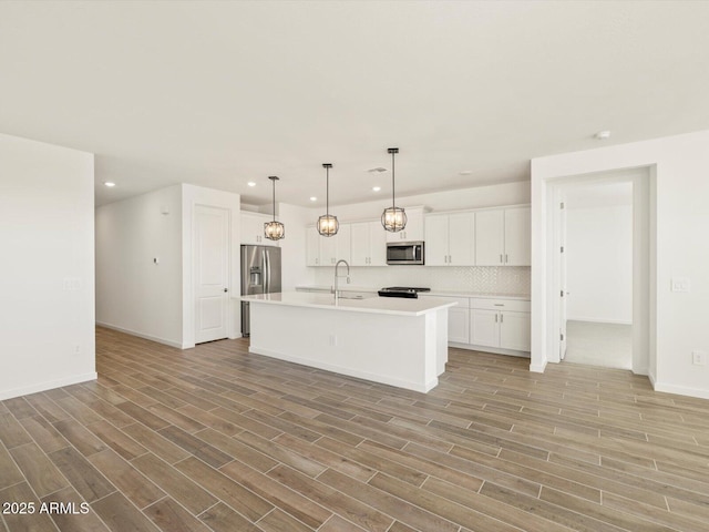 kitchen with white cabinets, pendant lighting, decorative backsplash, a kitchen island with sink, and appliances with stainless steel finishes