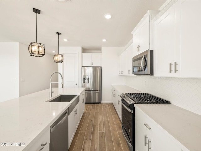 kitchen with appliances with stainless steel finishes, hanging light fixtures, light stone counters, white cabinets, and sink