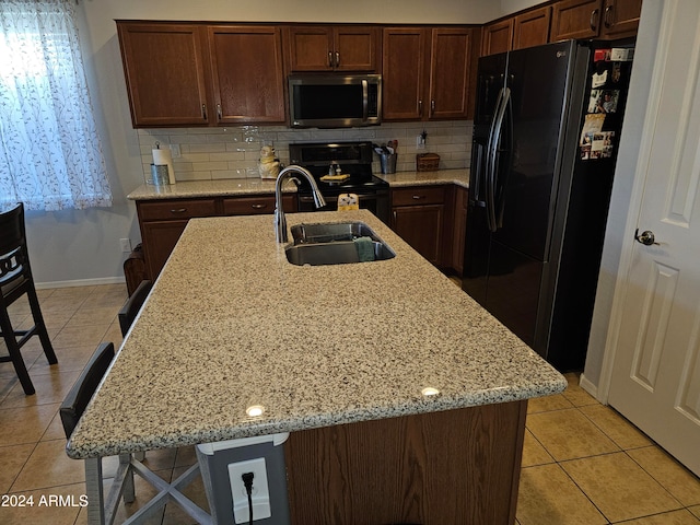 kitchen with a kitchen island with sink, a breakfast bar, black appliances, and light stone counters