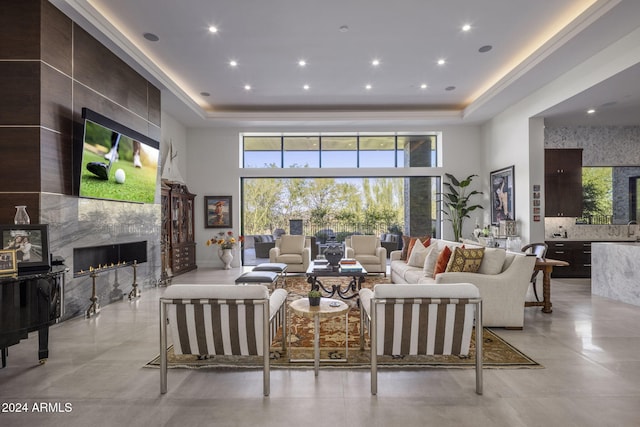 living room with a towering ceiling, a high end fireplace, tile walls, and a raised ceiling