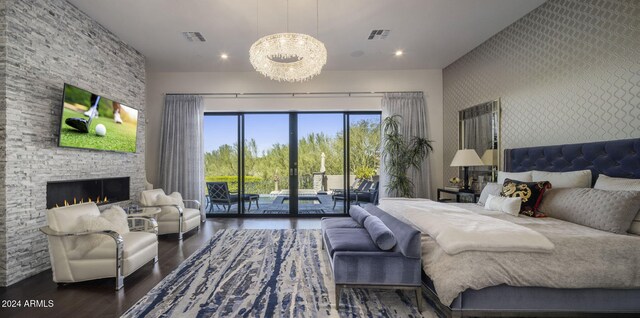 bedroom featuring a stone fireplace, access to exterior, an inviting chandelier, and dark hardwood / wood-style flooring