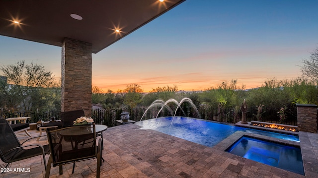 pool at dusk with a patio, pool water feature, and an in ground hot tub