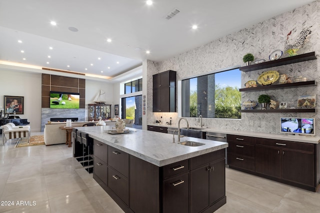 kitchen featuring sink, a fireplace, dark brown cabinetry, stainless steel dishwasher, and a kitchen island with sink